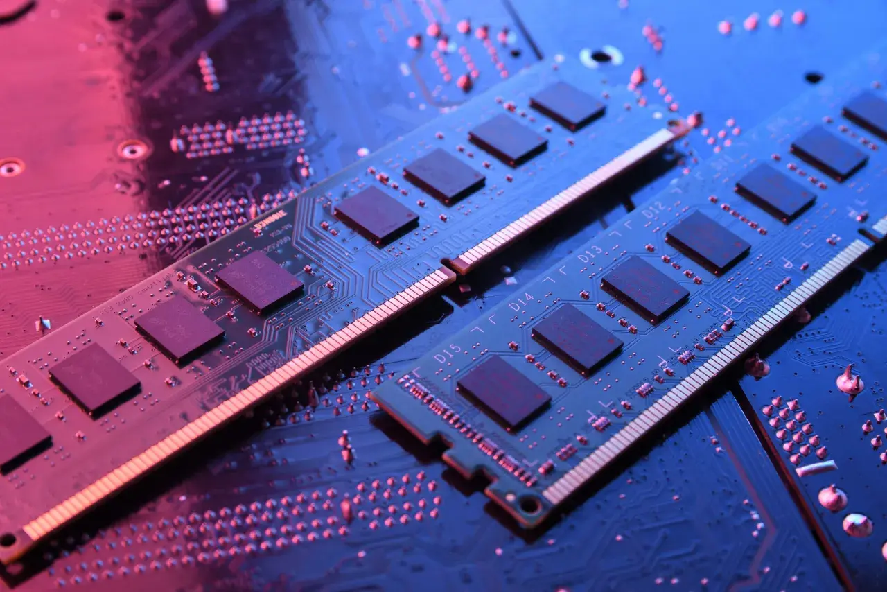 Dwa moduły RAM do laptopa leżą na płycie głównej, oświetlone niebieskim i różowym światłem.