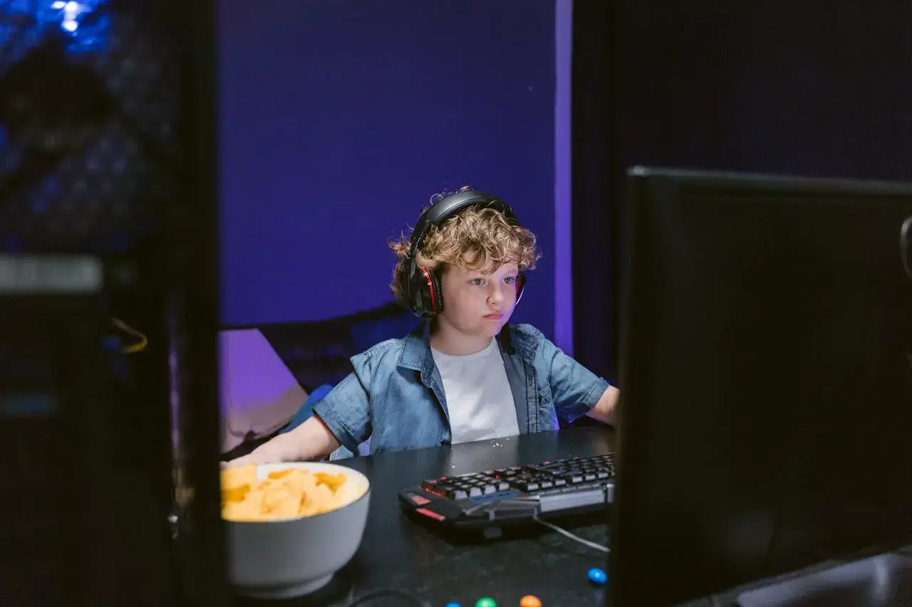 Chłopiec w słuchawkach gra w Roblox na przeglądarce, obok miska chipsów.