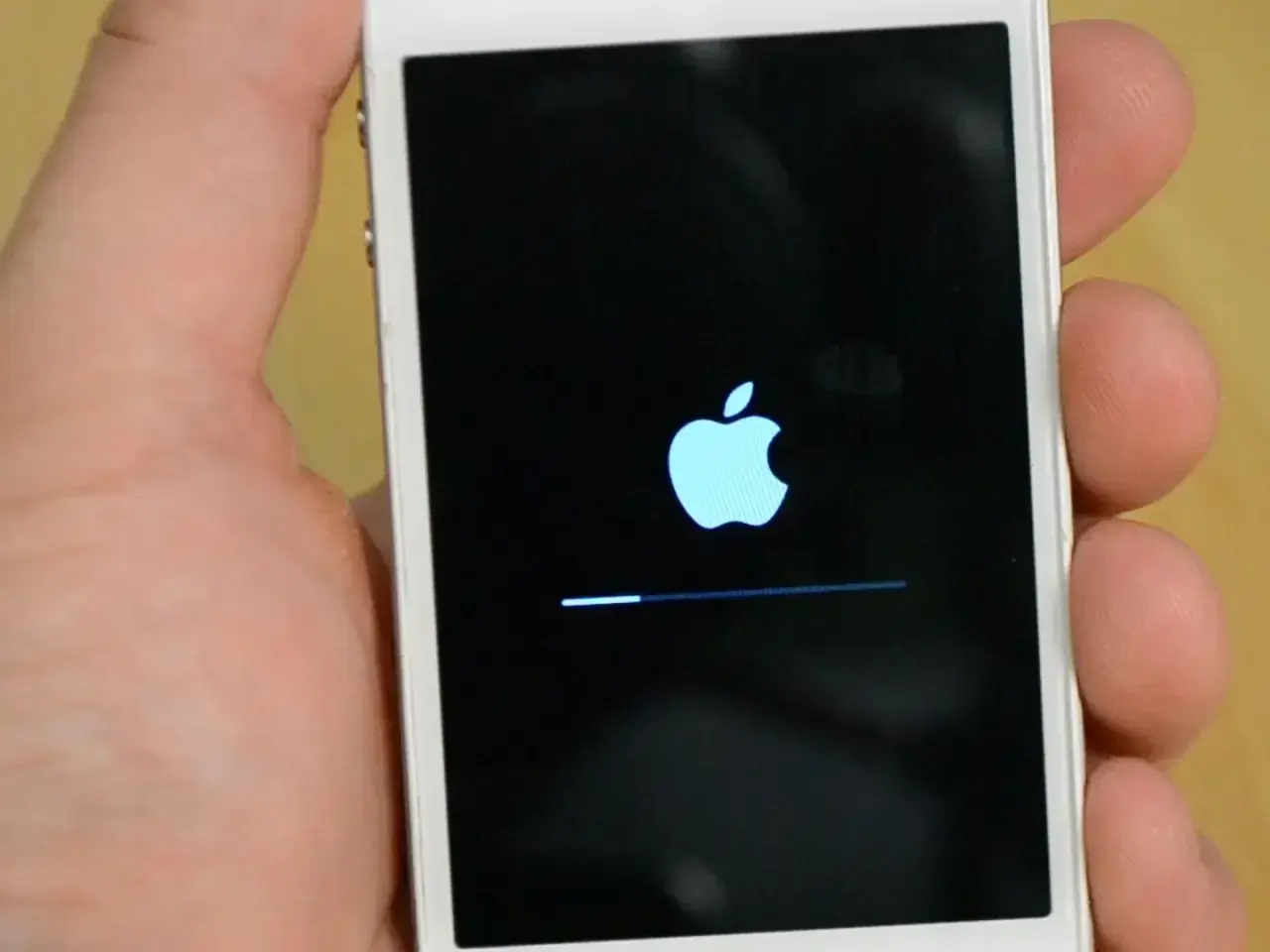 Dłoń trzyma biały iPhone z logo Apple i paskiem postępu. To ekran, który pojawia się, gdy próbujesz jak zresetować iPhone.