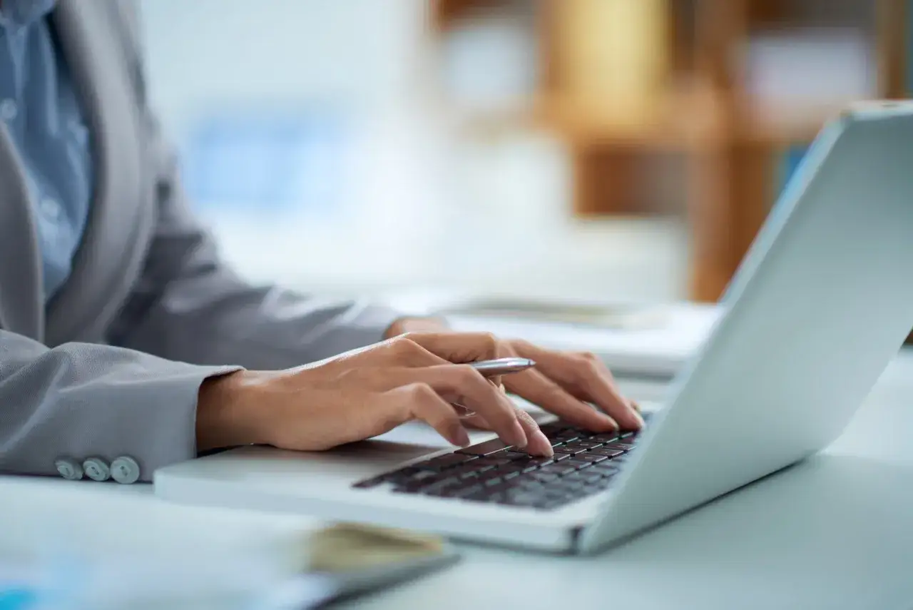 Dłonie piszą na klawiaturze laptopa, zastanawiając się, ile prądu zużywa laptop na godzinę.