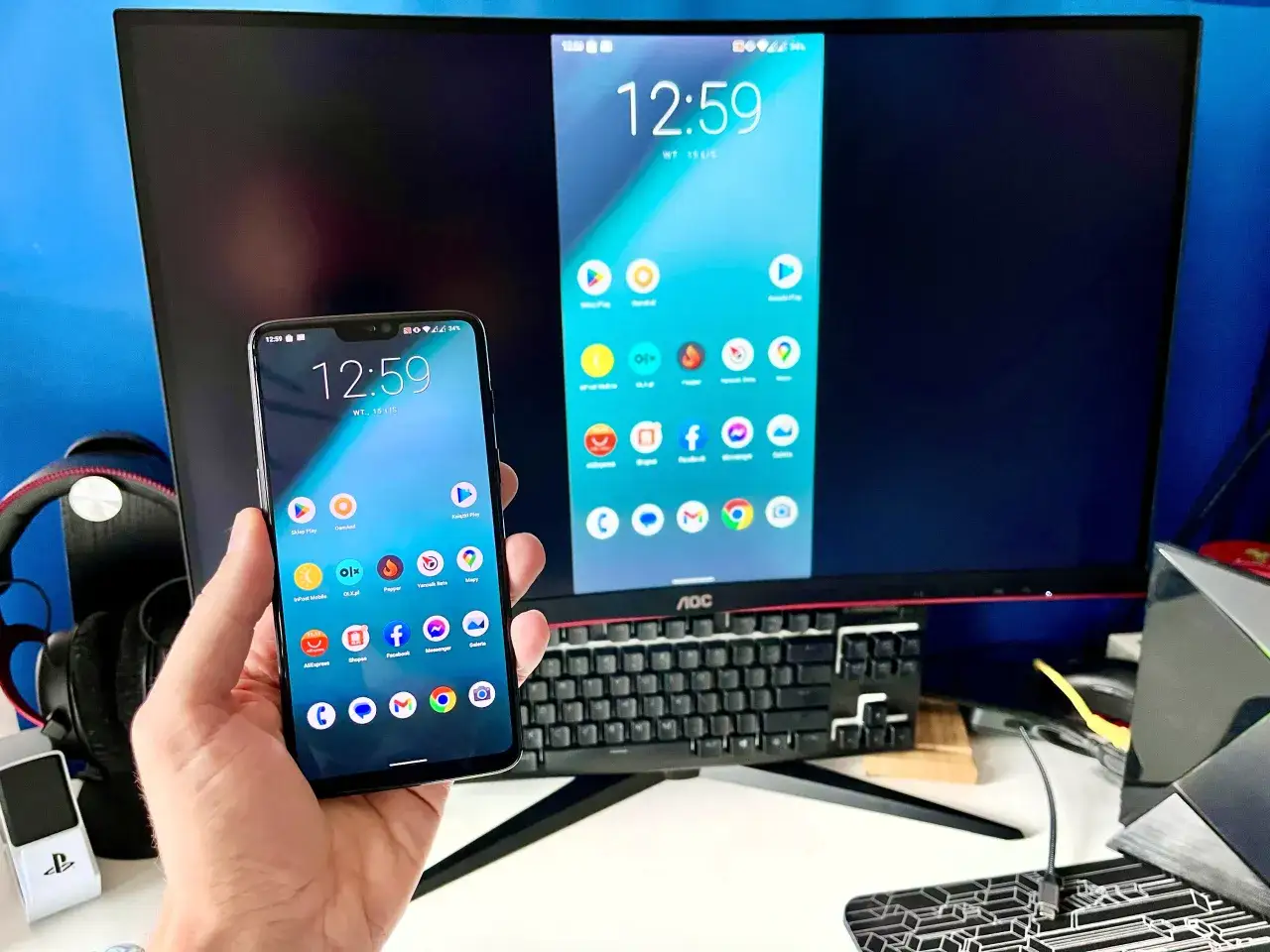 Smartfon z widocznymi ikonami aplikacji wyświetla ekran na dużym monitorze, pokazując, jak przenieść obraz z laptopa na telewizor bezprzewodowo.