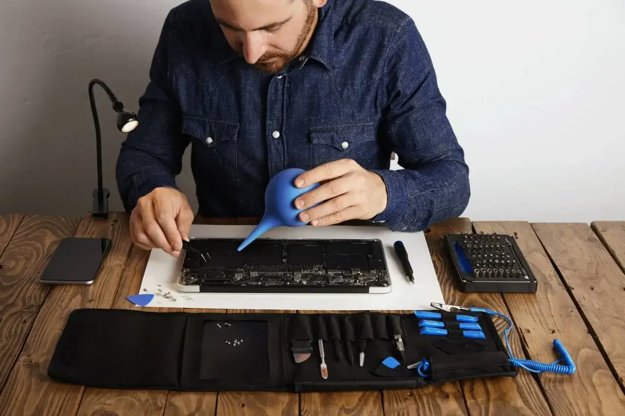 Mężczyzna czyści wnętrze laptopa, by rozwiązać problem, co zrobić żeby laptop się nie zacinał. Widać narzędzia do naprawy.