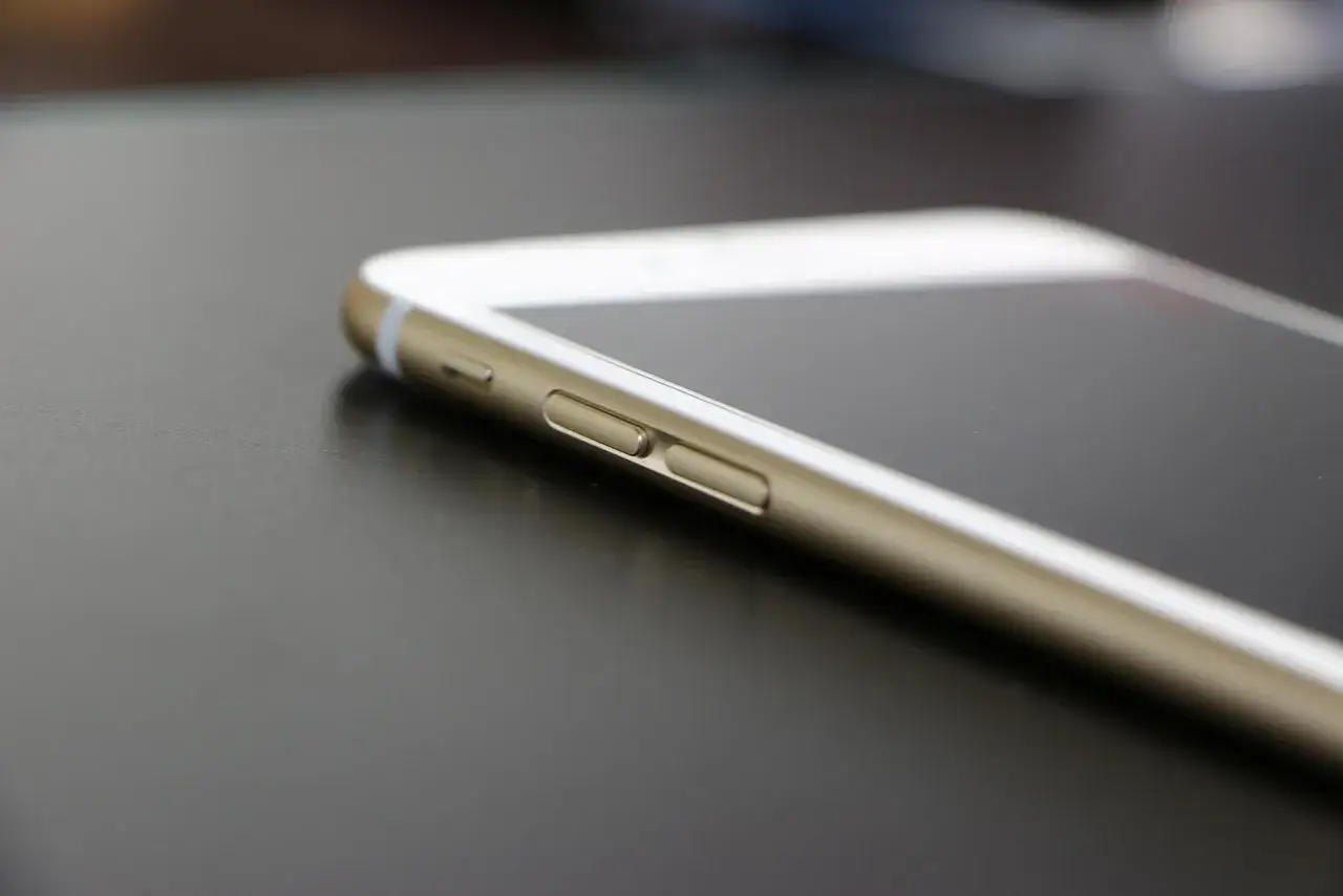 Złoty iPhone na ciemnym tle. Dowiedz się, jak zablokować iPhone, naciskając przyciski boczne.
