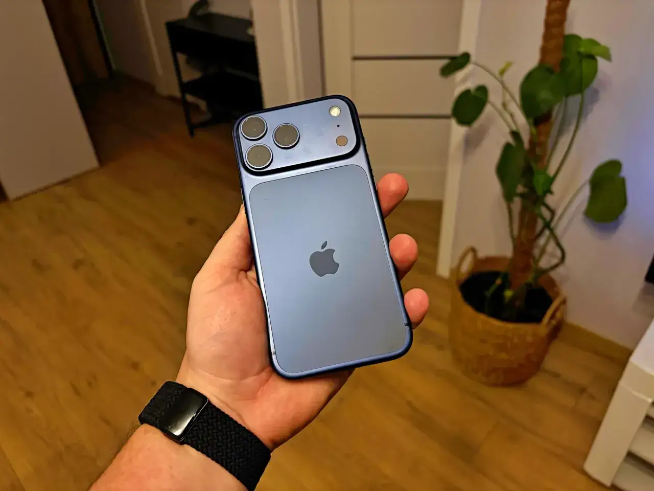 Dłoń trzyma granatowy iPhone z trzema obiektywami. Zastanawiasz się, ile kosztuje iPhone?