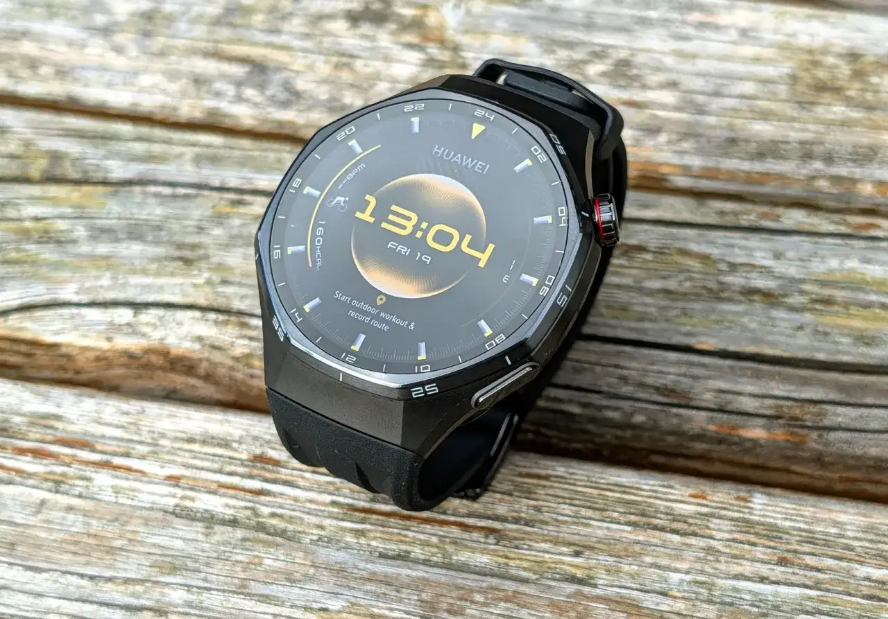 Czarny smartwatch Huawei na drewnianym blacie. Ekran pokazuje godzinę 13:04 i datę. Dowiedz się, jak zaktualizować Huawei Watch, by cieszyć się nowymi funkcjami.