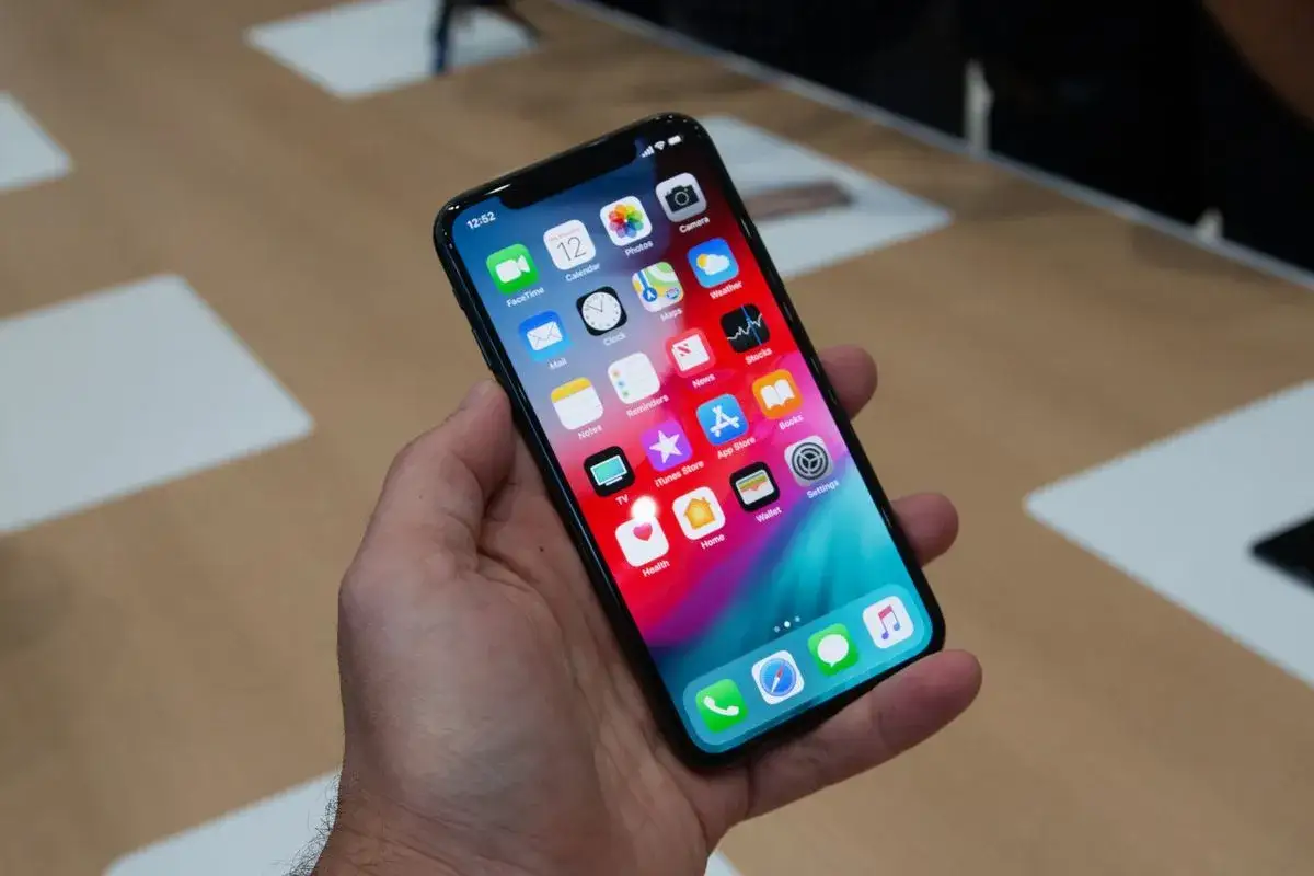 Dłoń trzyma smartfon z kolorowym ekranem, na którym widać ikony aplikacji. Czy to iPhone X czy XS?