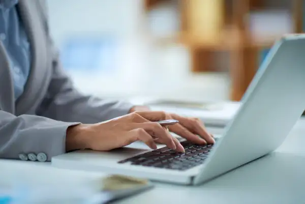 Dłonie piszą na klawiaturze laptopa, zastanawiając się, ile prądu zużywa laptop na godzinę.