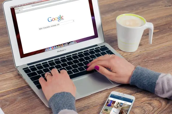 Kobieta pisze na laptopie, szukając w Google informacji, jak zmienić przeglądarkę. Obok stoi kubek kawy i telefon.