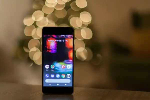 Smartfon z kolorową tapetą i ikonami aplikacji na tle rozmytych światełek.