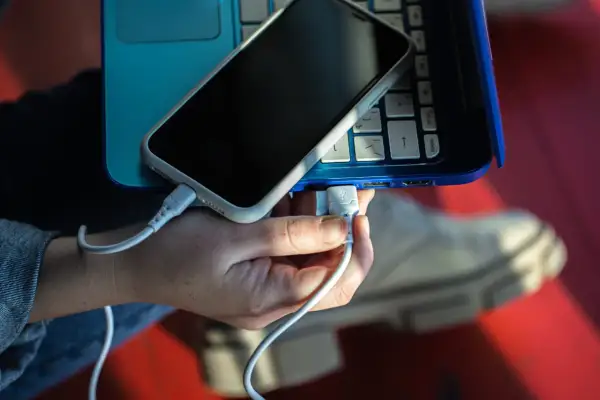 Dłoń podłącza kabel USB telefonu do laptopa, pokazując, jak połączyć telefon z laptopem.